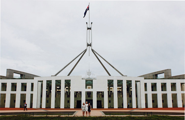 Three female students standing in front of Canberra's Parliament House