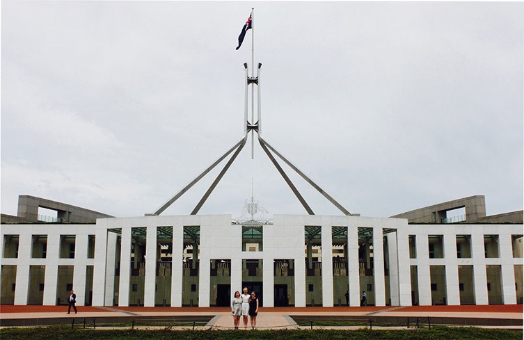 Three female students standing in front of Canberra's Parliament House