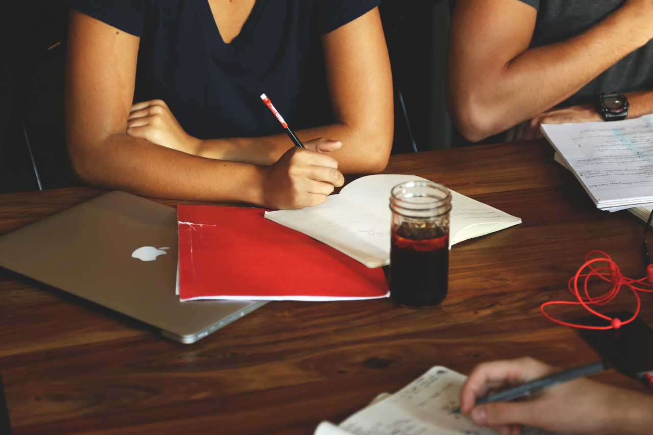 Person sitting at a table with a laptop, notebooks and drink in front of them