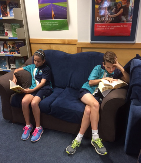 Two students sitting on a lounge in the library reading books