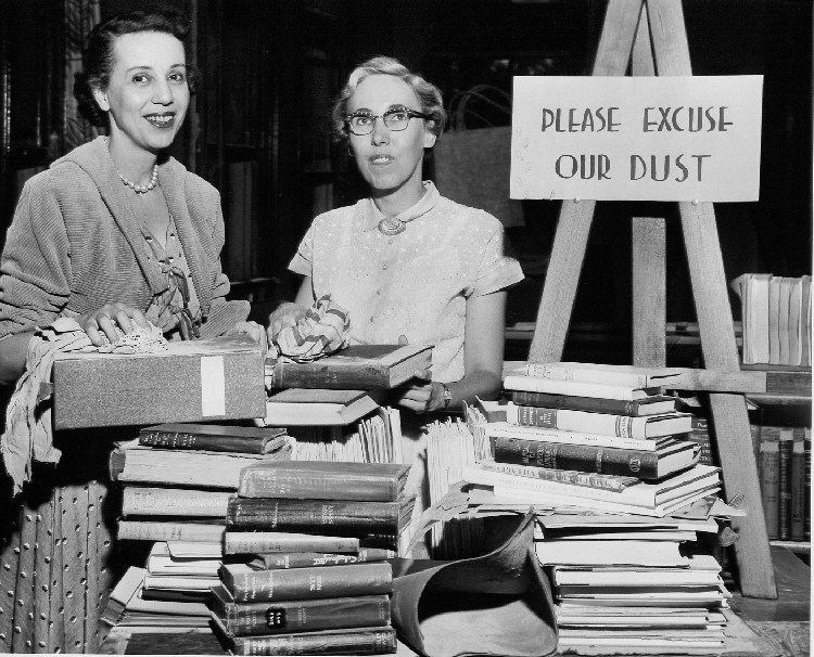 Black and White photograph of two librarians with piles of books in front of them.