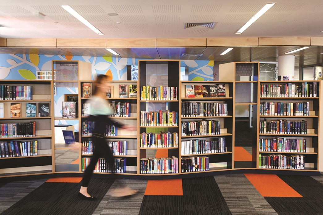 Teacher walking past bookshelves in a library