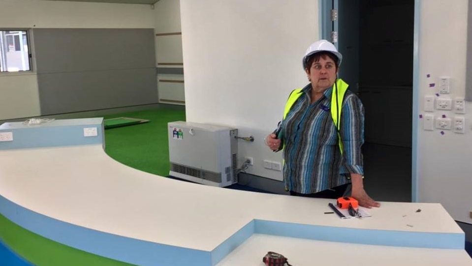 Teacher wearing hard hat and high-vis vest standing in a building site that will be a library.