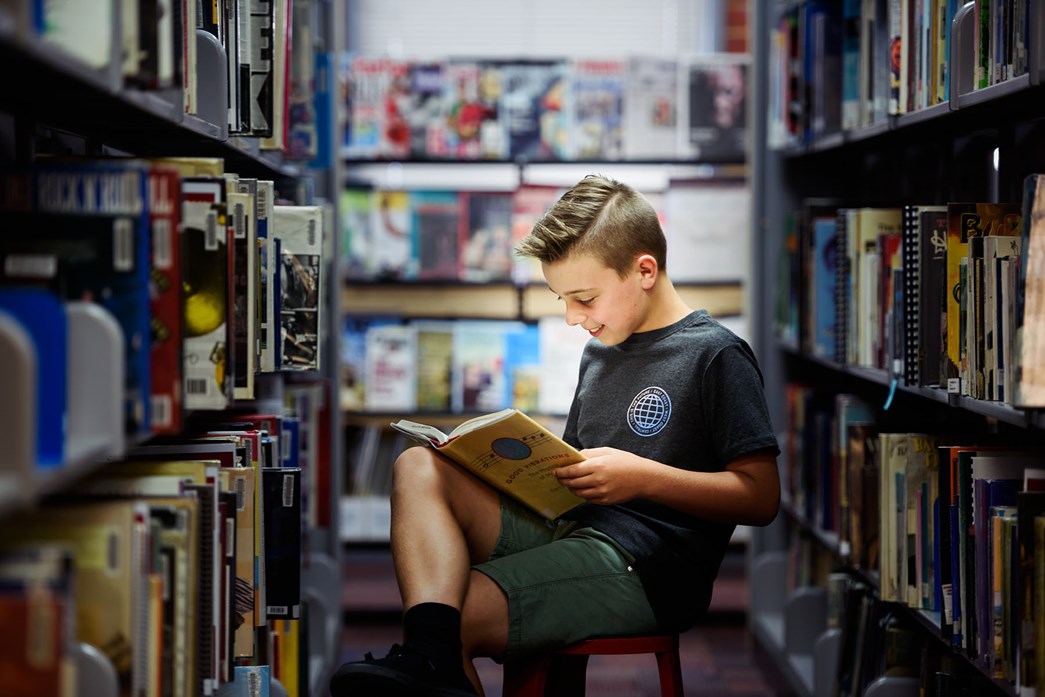 Young boy reading a book among the library shelves