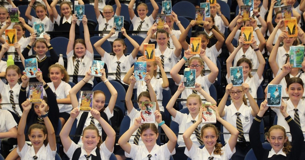 Students from Mt St Michael's College sitting in the gymnasium stands and holding books above their heads
