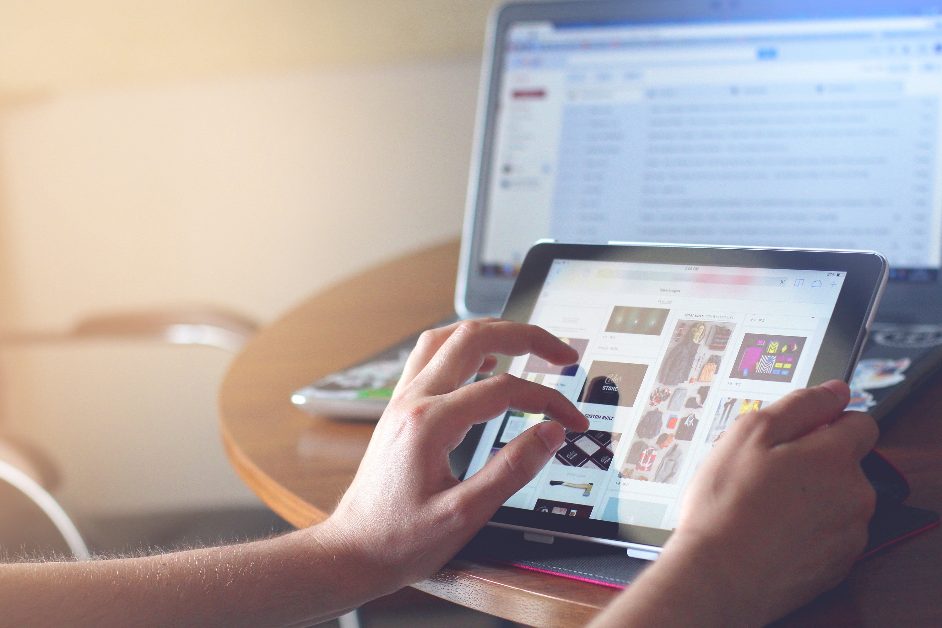 A person using a tablet to search images in front of an open laptop