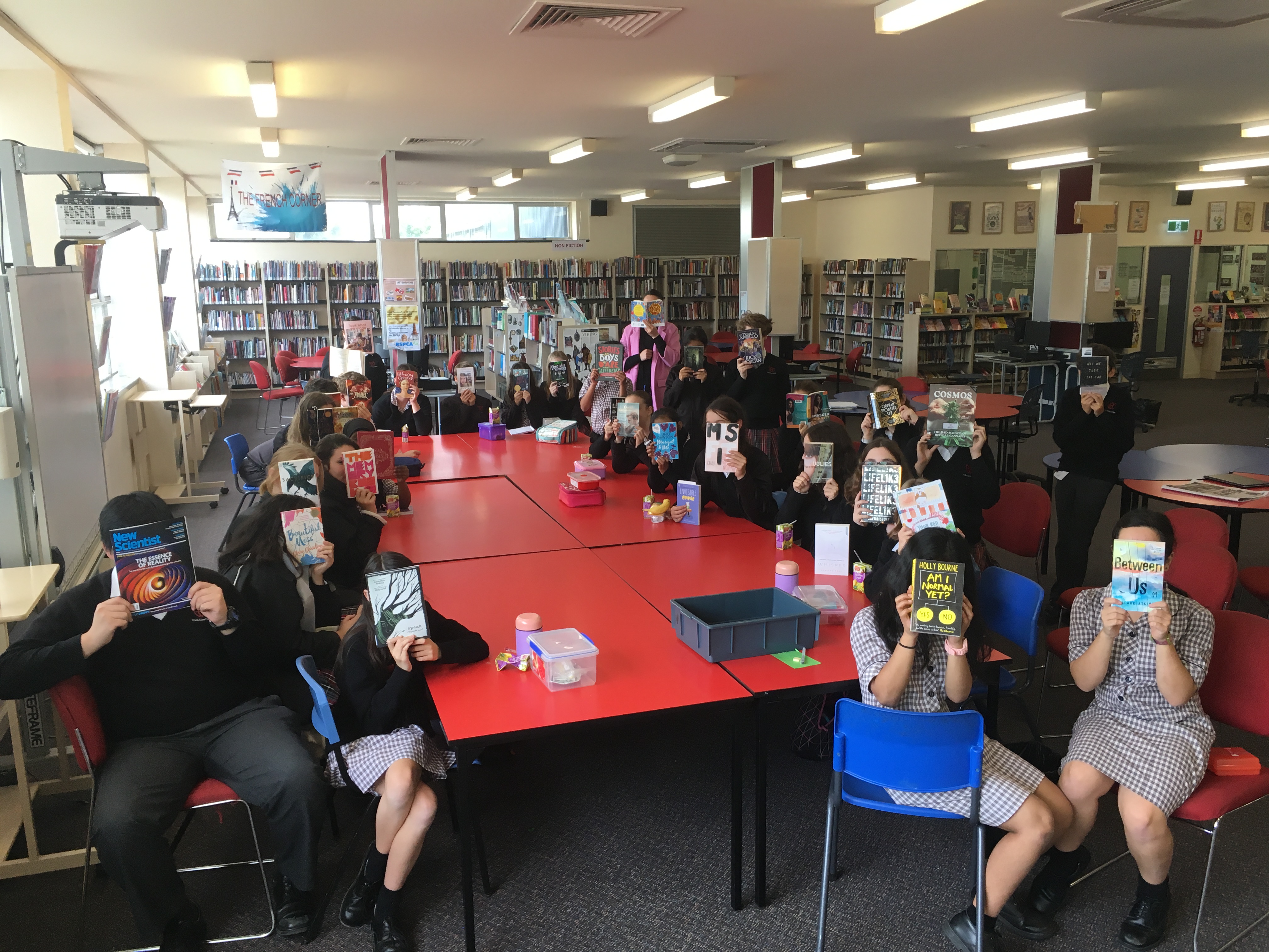 A group of students in a library holding up books in front of their faces