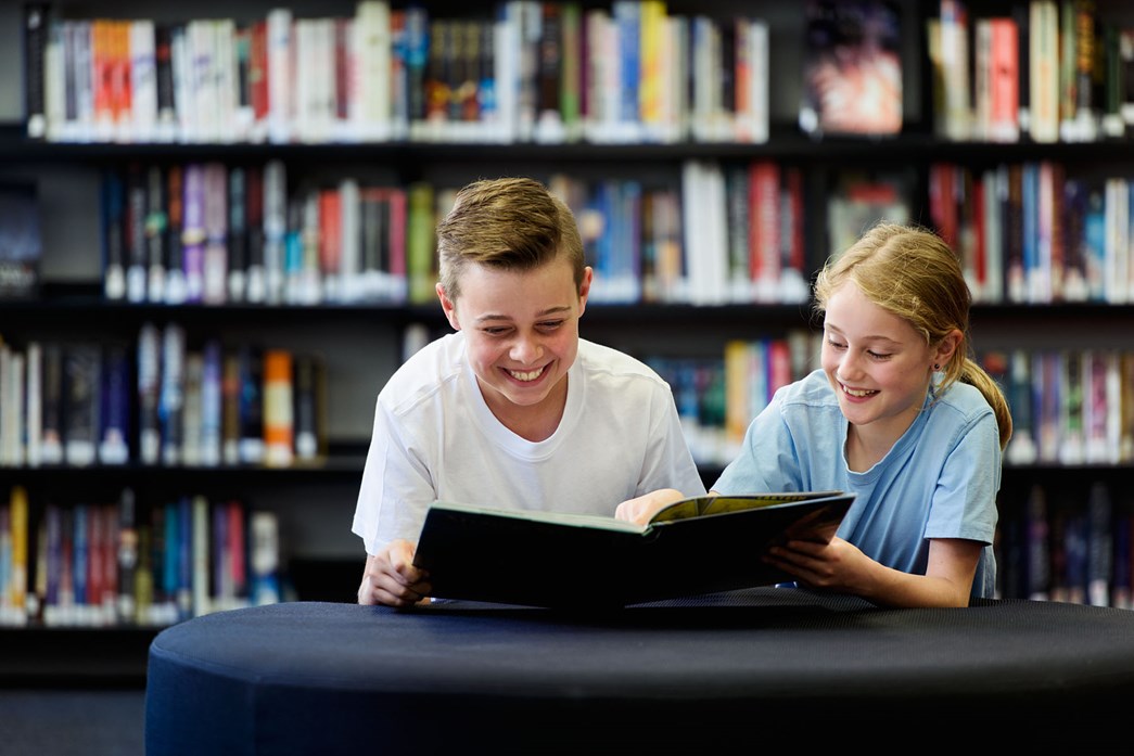 Two children in a library reading a book together