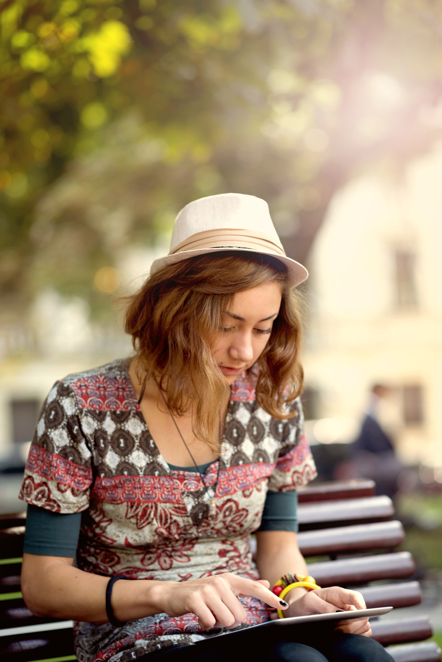 Girl sitting on a park bench outside reading an e-book