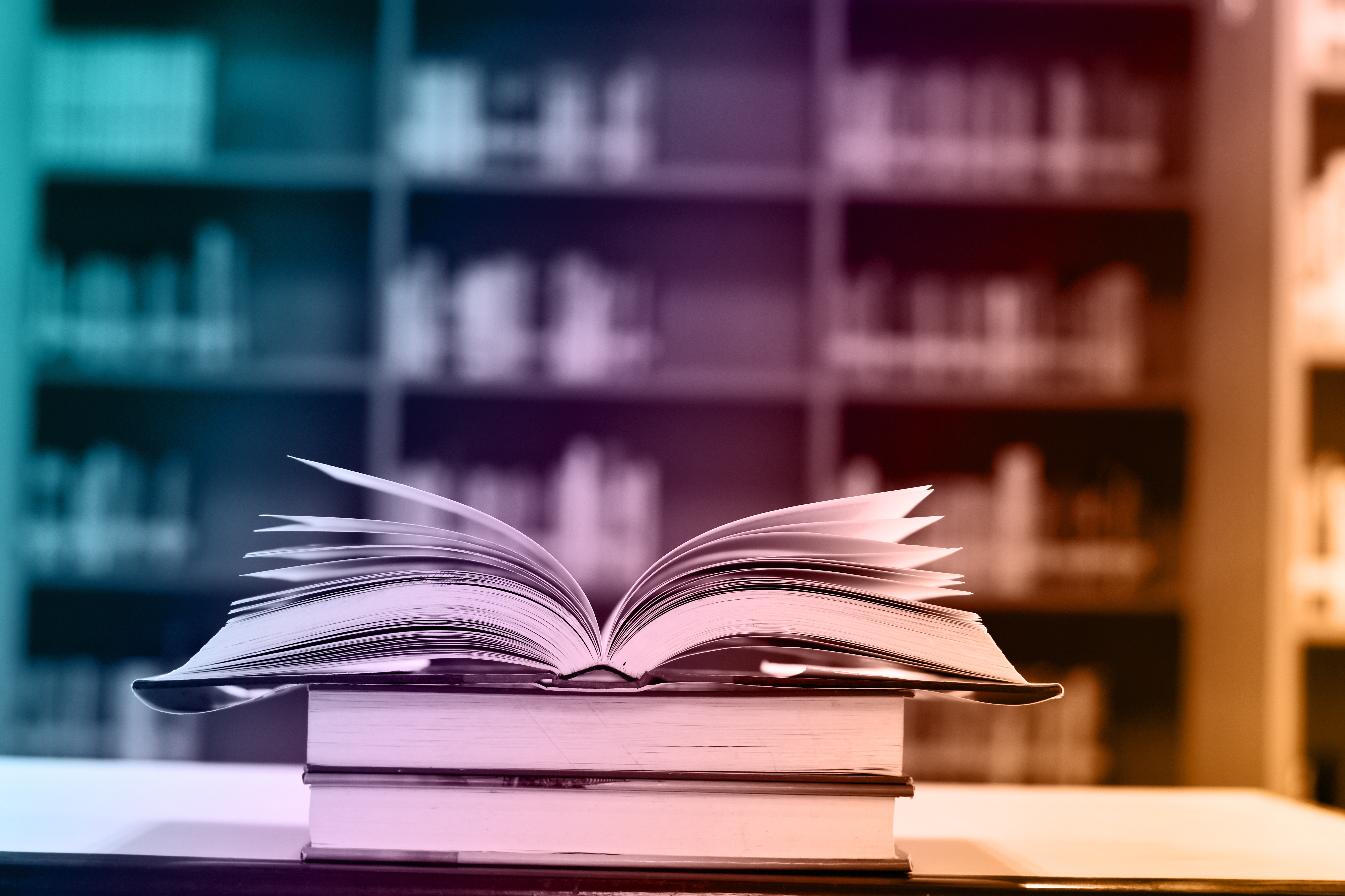 Open book in front of bookshelves with a rainbow hue over the top