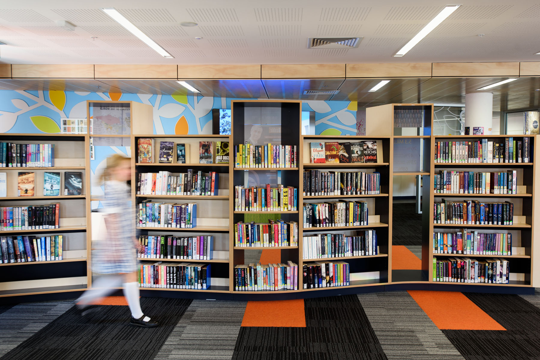 Girl walking by bookshelves in a school library